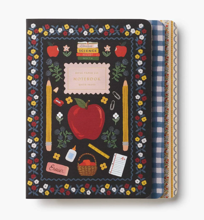 A School themed notebook with a black cover decorated with a colorful floral border, red apple, yellow pencils, and school supplies. The notebook is shown closed with its patterned paper covers partially visible on the right side. Available at Be Charmed