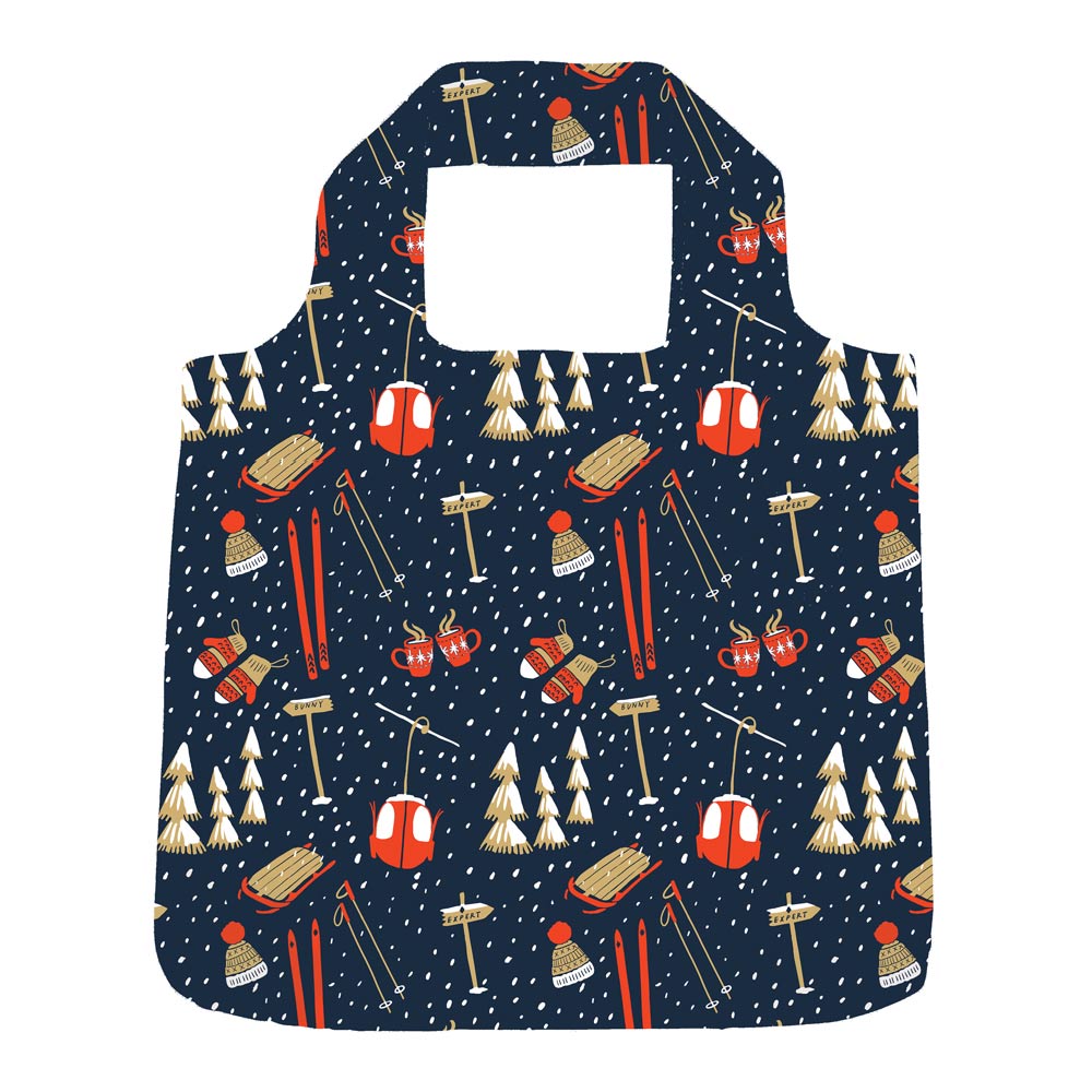 A reusable folding shopping bag with a dark navy blue background and a winter ski pattern featuring red gondolas, orange ski boots, white pine trees, and skis, shown on a plain white background. Available at Be Charmed