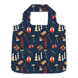 A reusable folding shopping bag with a dark navy blue background and a winter ski pattern featuring red gondolas, orange ski boots, white pine trees, and skis, shown on a plain white background. Available at Be Charmed