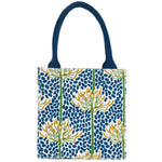 A tote bag with dark blue handles and a blue, yellow, and green botanical pattern on a white background. Available at Be Charmed
