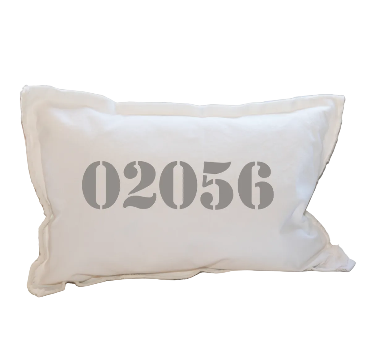 A beige lumbar pillow with the zip code '02056' printed in a large, bold font, resting on a white sofa. Available at Be Charmed