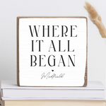 A rustic marlin wooden block with the text 'WHERE IT ALL BEGAN' and 'Medfield' printed on it, displayed on a stack of books. Availble at Be Charmed