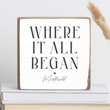 A rustic marlin wooden block with the text 'WHERE IT ALL BEGAN' and 'Medfield' printed on it, displayed on a stack of books. Availble at Be Charmed