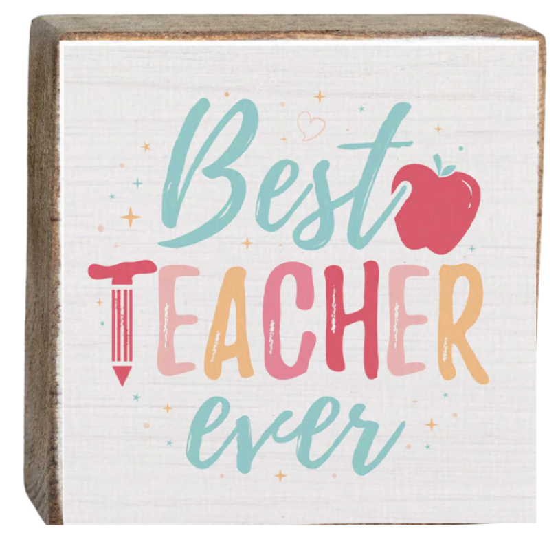 A decorative wooden block with 'Best Teacher Ever' printed on it, featuring multicolored text and a red apple symbol. Available at Be Charmed