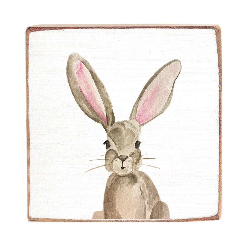 A decorative wooden block with a rustic painting of a bunny with long ears in brown and pink colors. Available at Be Charmed