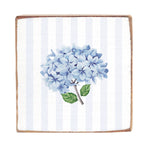 A decorative wooden block featuring a printed design with blue hydrangea flowers on a striped background. Available at Be Charmed