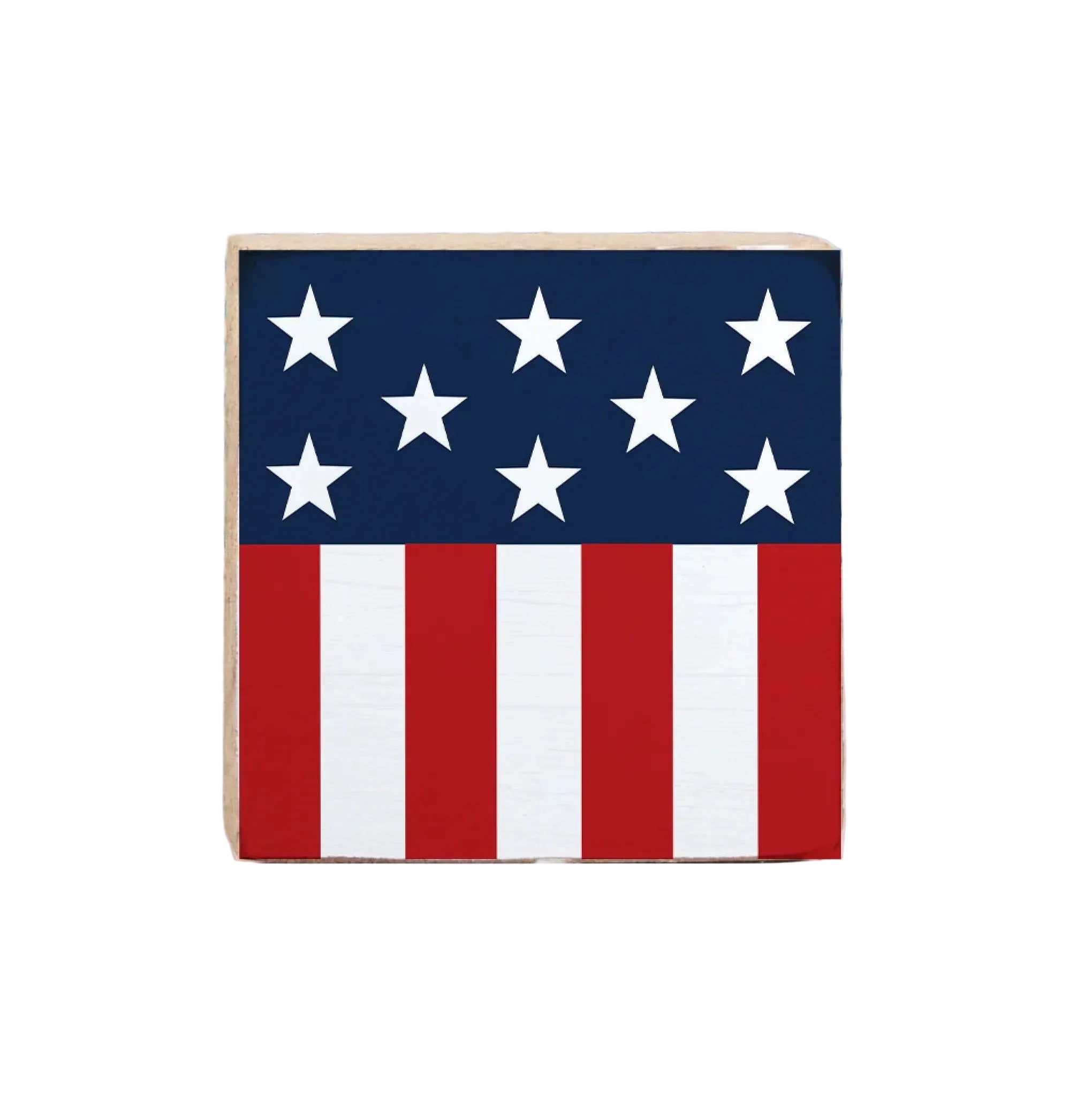 A decorative wooden block sign featuring the American flag in red, white, and blue colors, placed on a surface with a blue patterned background. Available at Be Charmed