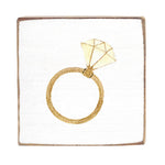 A gold-colored ring-shaped solitaire brooch displayed on a white square rustic block. Available at Be Charmed