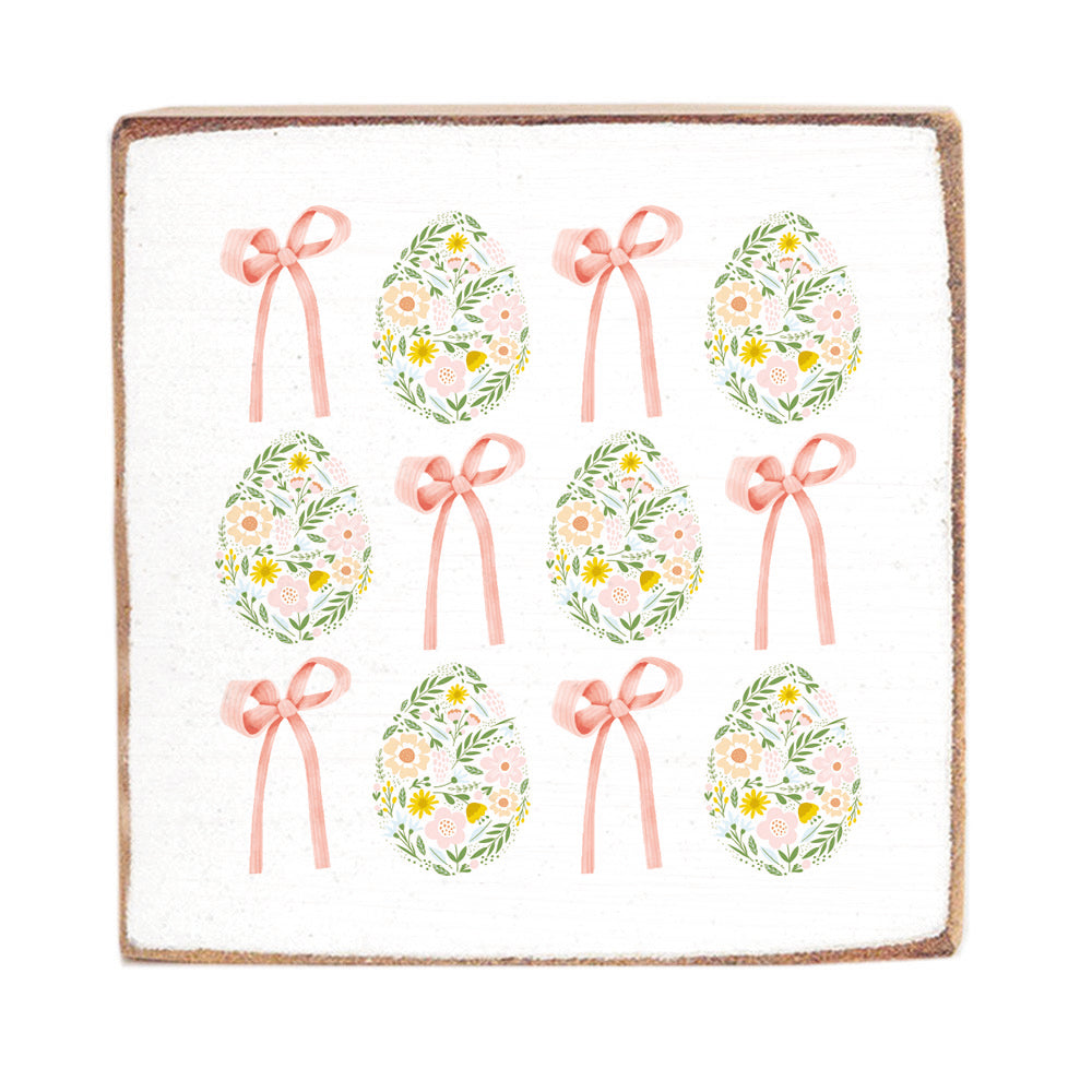 A decorative Rustic Marlinwooden block with Easter egg patterns and bows in vintage colors. Available at Be Charmed