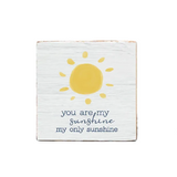 A decorative wooden block with a sun illustration and the text 'you are my sunshine my only sunshine' on it, placed on a wooden surface. Available at Be Charmed