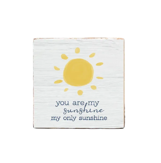A decorative wooden block with a sun illustration and the text 'you are my sunshine my only sunshine' on it, placed on a wooden surface. Available at Be Charmed