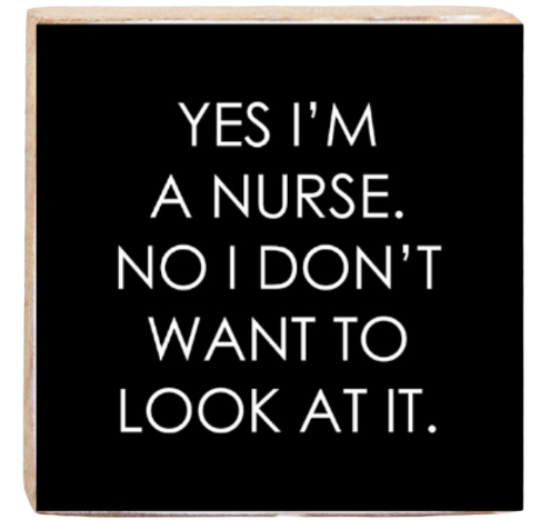 A wooden decorative block with the phrase 'YES I'M A NURSE. NO I DON'T WANT TO LOOK AT IT.' printed on it in black and white. Available at Be Charmed