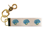 A beige cotton keychain with a floral pattern, featuring blue hydrangea designs, attached to a gold-toned metal clasp. Available at Be Charmed