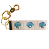 A beige cotton keychain with a floral pattern, featuring blue hydrangea designs, attached to a gold-toned metal clasp. Available at Be Charmed
