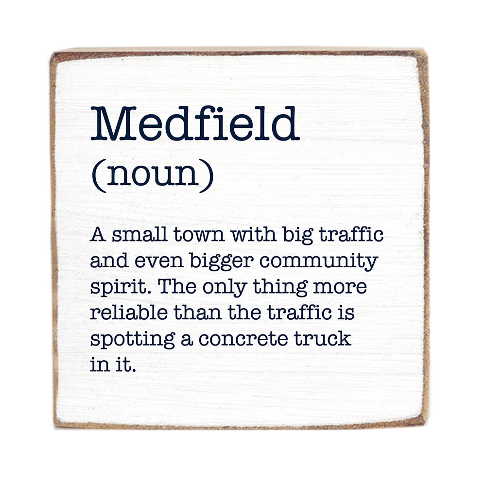 A wooden block with the definition of 'Medfield' printed on it, stating it's a small town with big traffic and community spirit. Available at Be Charmed