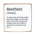 A wooden block with the definition of 'Medfield' printed on it, stating it's a small town with big traffic and community spirit. Available at Be Charmed