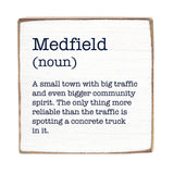 A wooden block with the definition of 'Medfield' printed on it, stating it's a small town with big traffic and community spirit. Available at Be Charmed