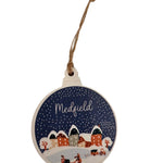 A round, rustic wooden ornament with a bulb design, featuring a vintage snow globe village scene in blue and white colors, with the word 'MEDField' written on it. Available at Be Charmed