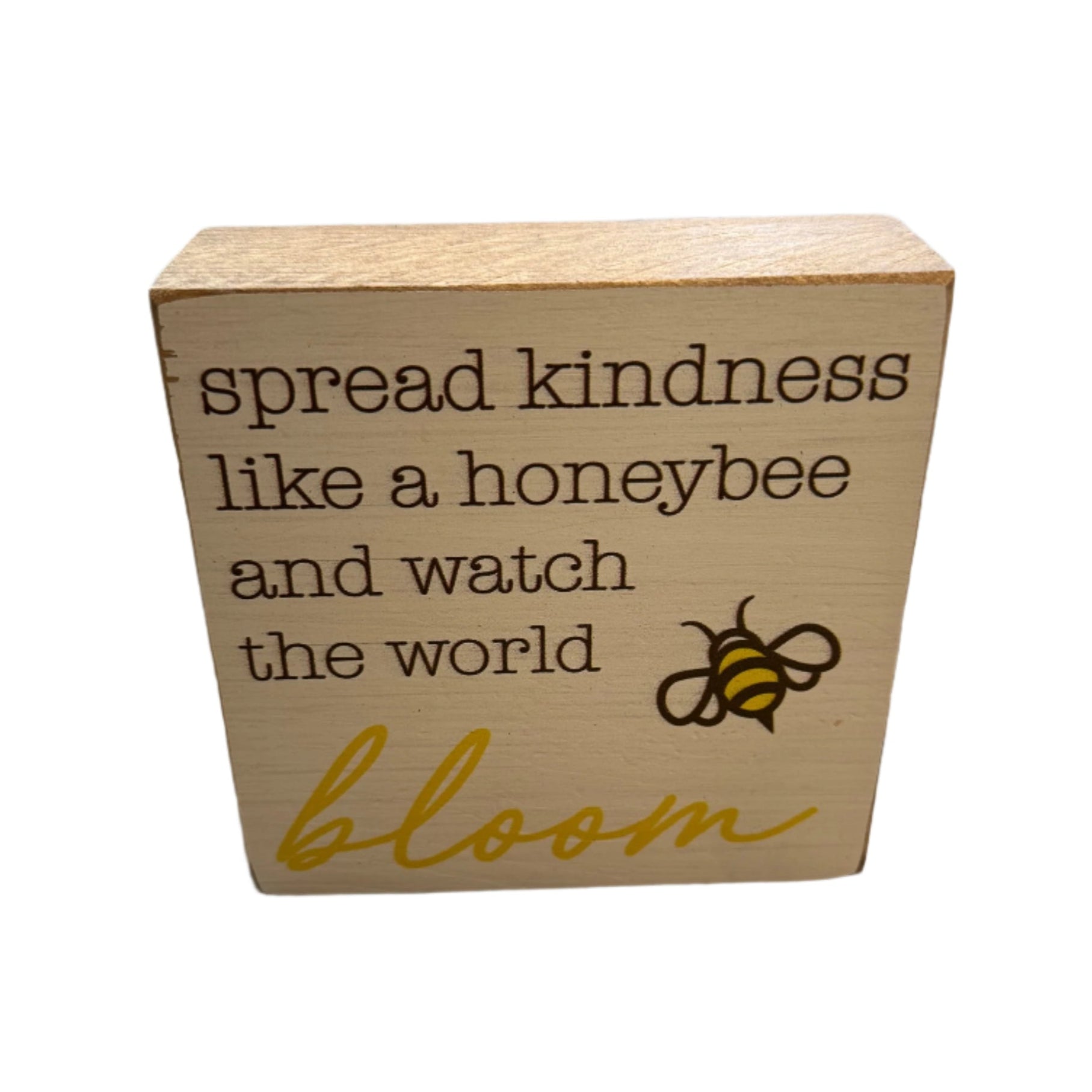 A beige wooden block with the phrase 'spread kindness like a honeybee and watch the world bloom' printed on it, along with an image of a honeybee. Available at Be Charmed