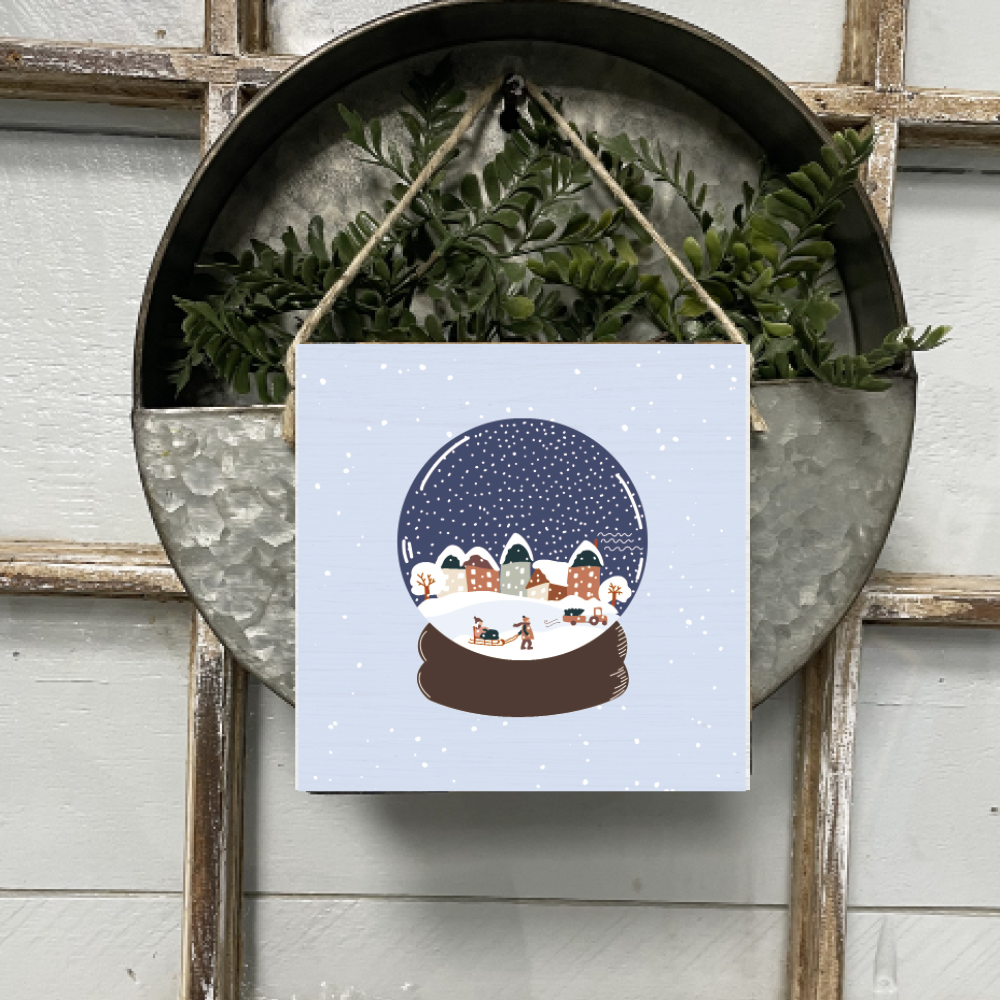 A Rustic Marlin square wooden sign with a vintage snow globe design, featuring a village scene, hung by a twine loop. Available at Be Charmed