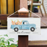 A rustic wooden twine sign featuring an illustration of a blue truck with carrots in the back, and the text 'Welcome' on a wooden post. Available at Be Charmed