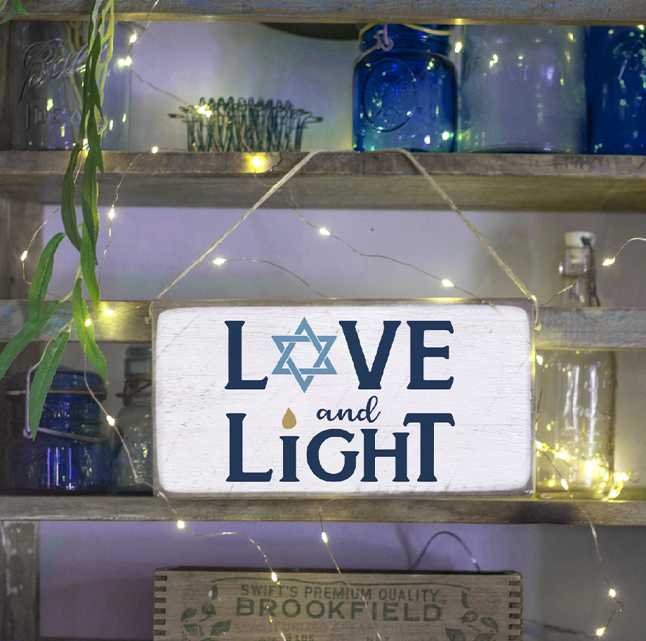 A rustic pine twine sign with 'Love and Light' written on it, hanging by a string of lights and blue bottles. Available at Be Charmed
