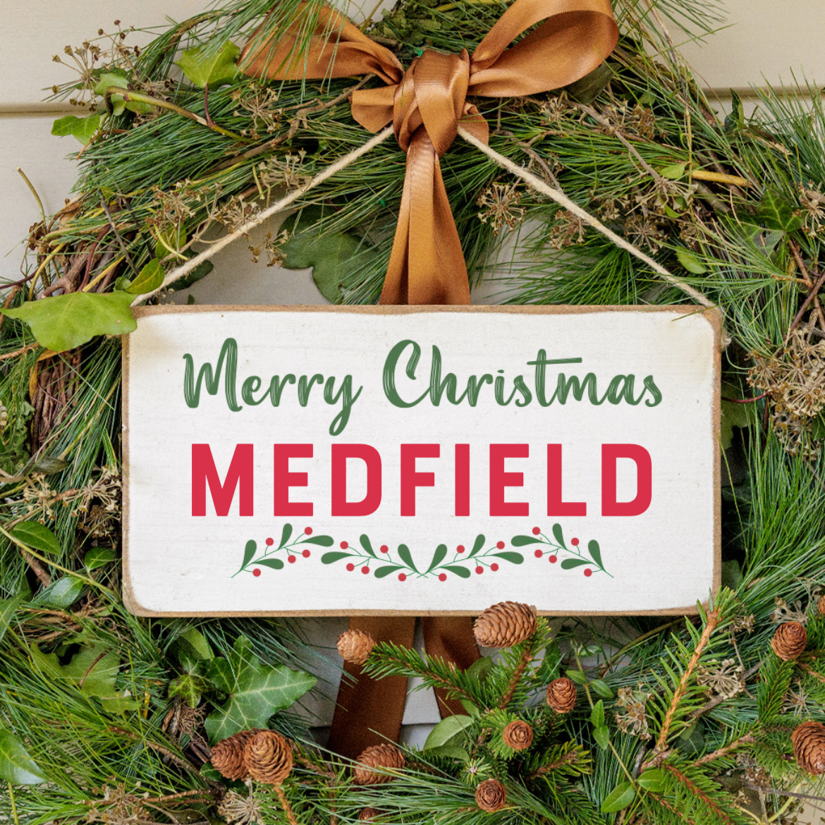 A rustic wooden sign with a 'Merry Christmas' message, green and red decorations, and pinecones. Available at Be Charmed