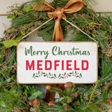 A rustic wooden sign with a 'Merry Christmas' message, green and red decorations, and pinecones. Available at Be Charmed
