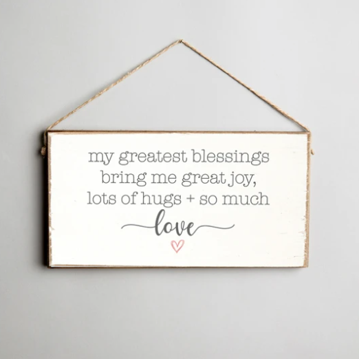 A rustic style twine hanging sign made of pine wood with the text 'My Greatest Blessings Bring Me Great Joy, Lots of Hugs + So Much Love' and a heart symbol. Available at Be Charmed