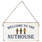 Decorative sign with 'Welcome to the Nuthouse' text and three nutcrackers on a white background. Available at Be Charmed