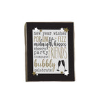 A decorative wooden block with a list of New Year's wishes written in a poetic format, accompanied by the word 'BUBBLY' at the bottom, indicating a celebratory tone. The block is dark in color with gold stars and a silver line drawing of a champagne bottle. Available at Be Charmed