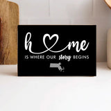 A black wooden block with white text and heart symbol, stating 'Home is where our story begins' with a small map outline representing Massachusetts. Available at Be Charmed