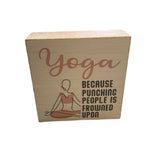 A decorative wooden block with 'Yoga Because Punching People is Frowned Upon' printed on it, featuring a simple illustration of a person in a yoga pose. Available at Be charmed