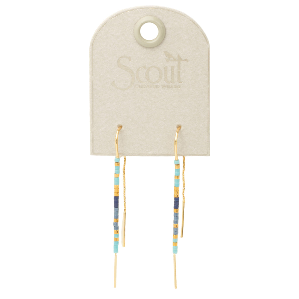 A pair of cobalt and gold colored earrings displayed on a card with 'Scout' branding. Available at Be Charmed