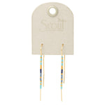 A pair of cobalt and gold colored earrings displayed on a card with 'Scout' branding. Available at Be Charmed
