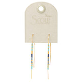 A pair of cobalt and gold colored earrings displayed on a card with 'Scout' branding. Available at Be Charmed