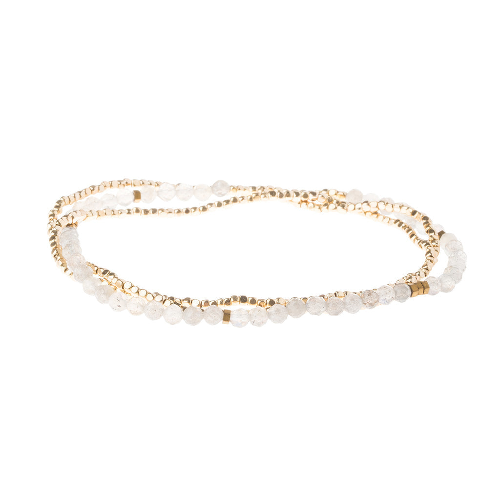 A delicate piece of jewelry featuring faceted gemstones and tiny geometric metal beads, capable of being wrapped as a bracelet or worn as a necklace. Available at Be Charmed