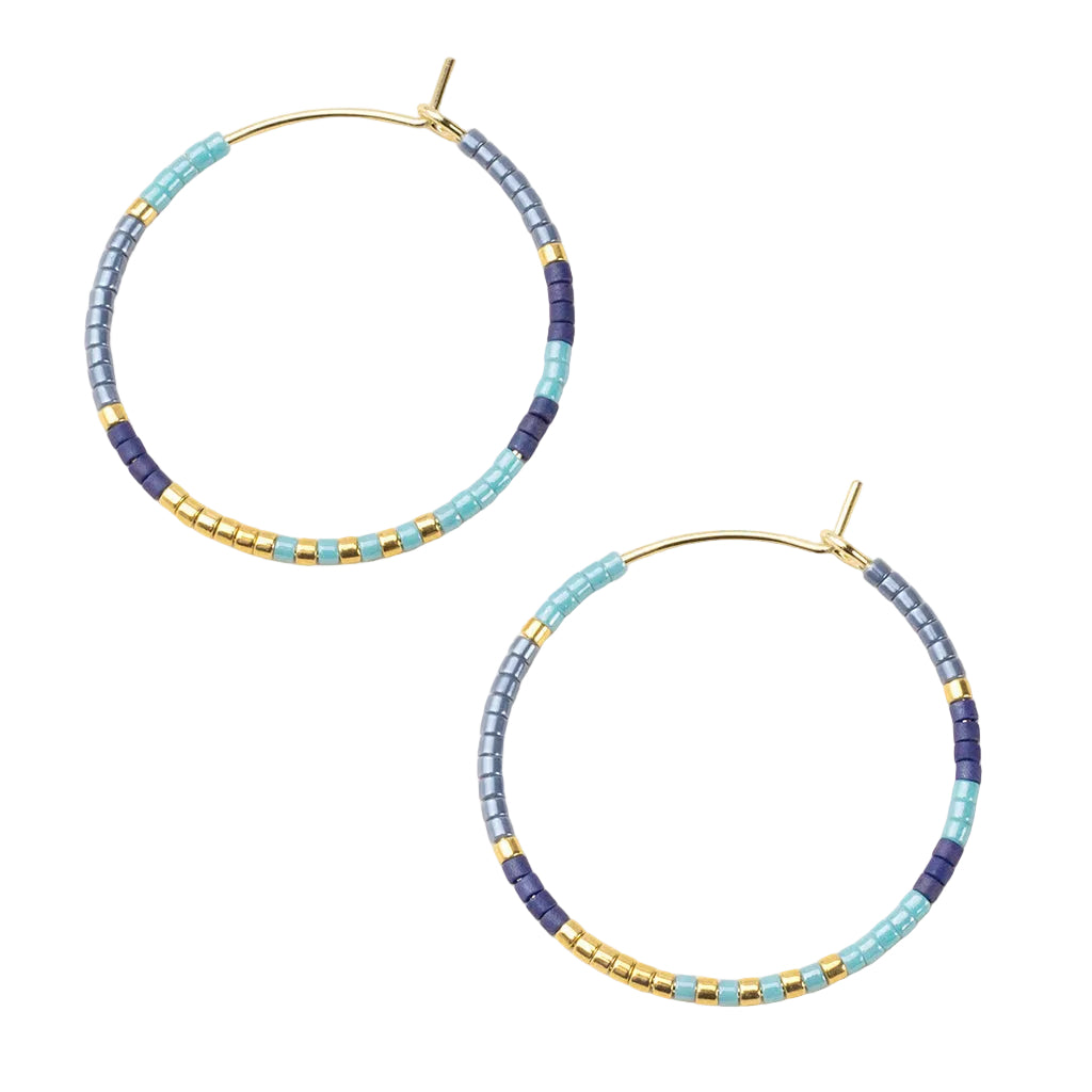 Pair of beaded hoop earrings with blue and gold colors on a beige background. Available at Be Charmed