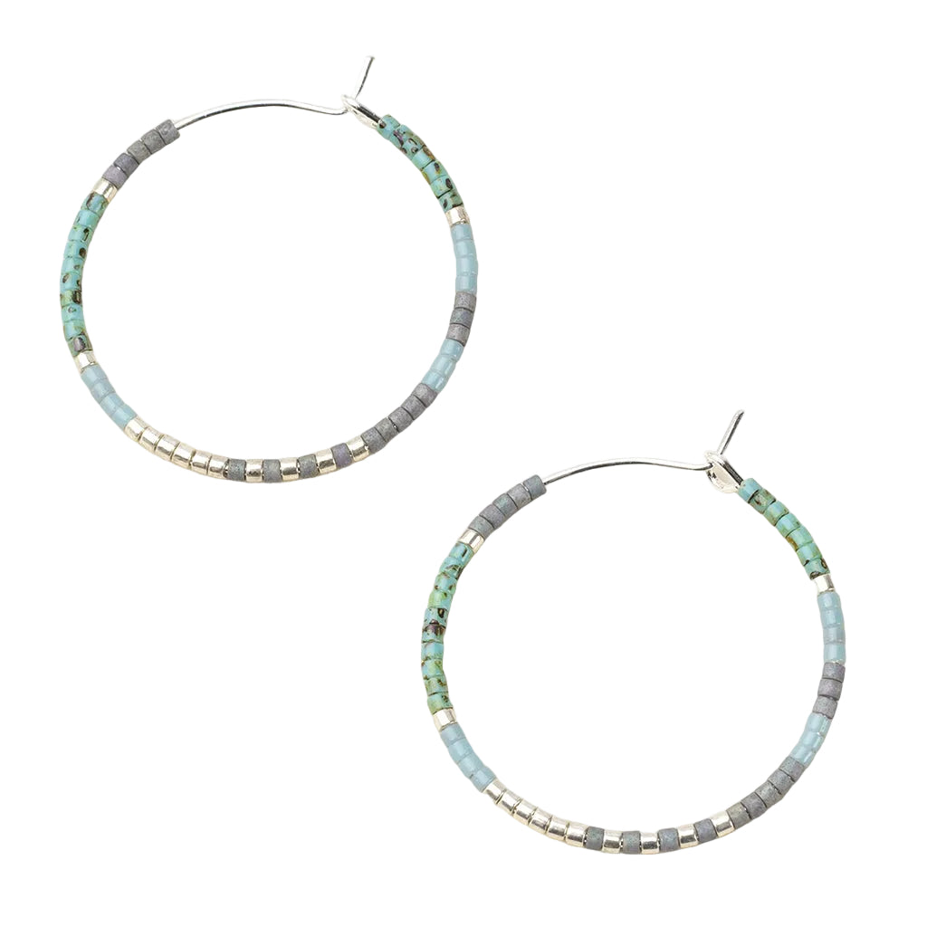 Pair of hoop earrings with turquoise and gray beads on a beige background. Available at Be Charmed
