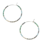 Pair of hoop earrings with turquoise and gray beads on a beige background. Available at Be Charmed