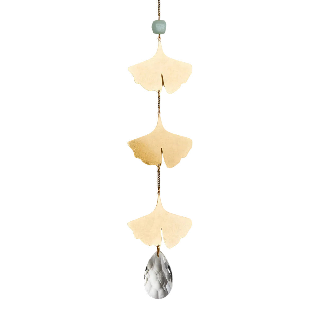 A brass suncatcher featuring three leaf-shaped cutouts and a crystal pendant hanging against a neutral background. Available at Be Charmed
