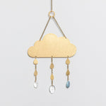 A brass suncatcher in the shape of a cloud with blue howlite gemstones and crystal pendants hanging from it. Available at Be Charmed