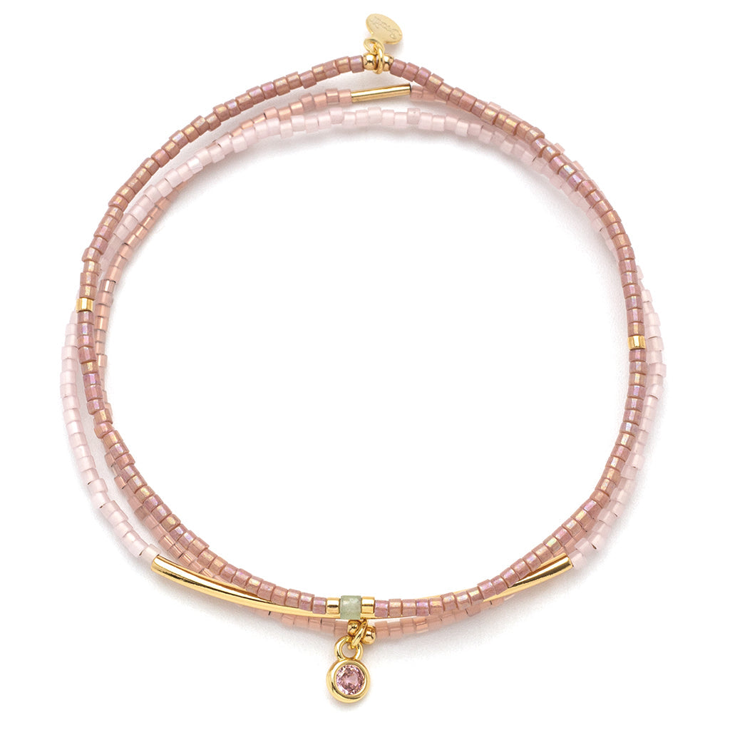 Pink beaded bracelet with gold accents and a pink gemstone charm on a white background. Available at Be Charmed