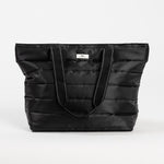 Black Puffer SCOUT Layover Tote – quilted puffer travel tote (19″ W × 13″ H × 5.5″ D), interior zipper compartments, reinforced bottom, folds flat. Available at Be Charmed