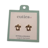 A pair of turtle-shaped stud earrings on a mint green and white card labeled 'cuties hypoallergenic surgical steel posts'. Available at Be Charmed