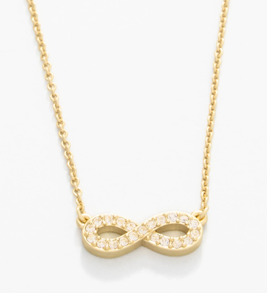 Gold infinity necklace on a white background. Available at Be Charmed