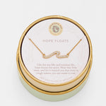 Gold necklace in a round jewelry box with 'Hope Floats' text on a light background. Available at Be Charmed