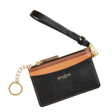Black and brown wallet with strap and keychain on beige background. Available  at Be Charmed