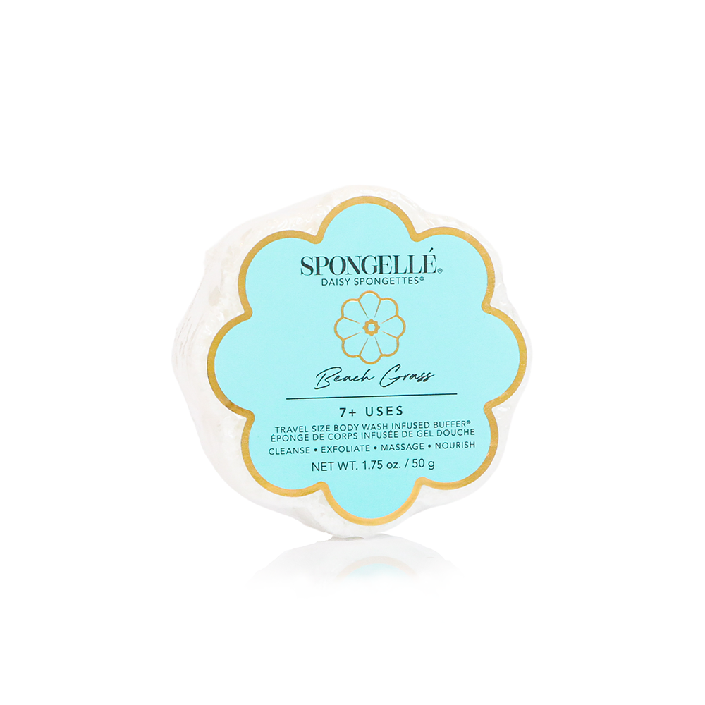 A Spongellé branded bath sponge in the shape of a flower, predominantly white with yellow accents and text detailing the product name and usage information. Available at Be Charmed