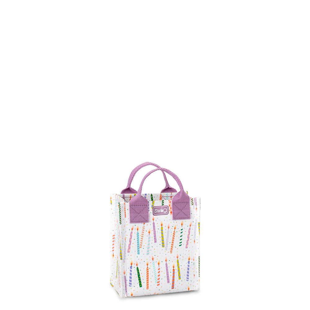 A mini reusable gift bag with a multicolored geometric pattern and purple handles. Available at Be Charmed